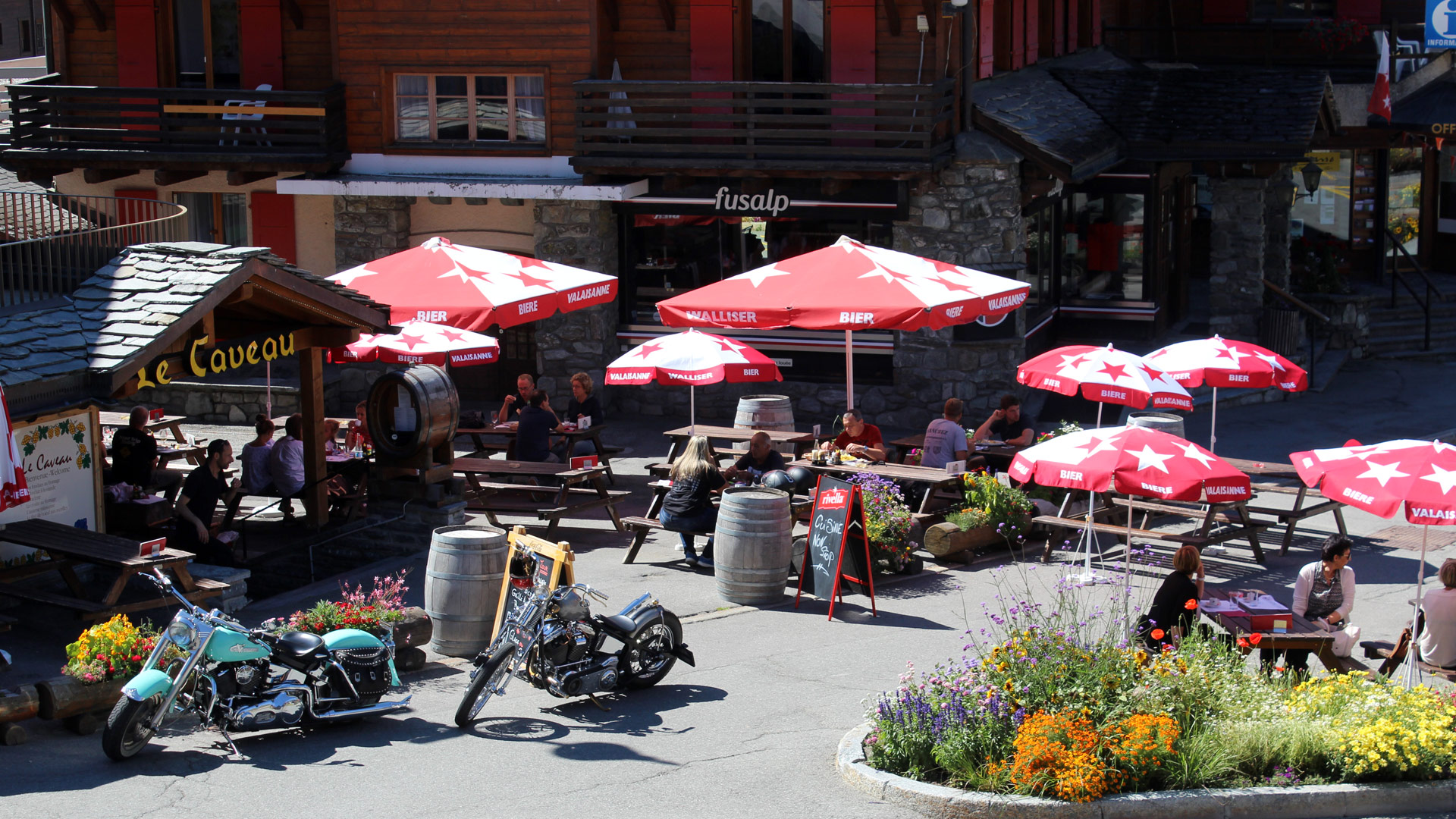 La terrasse ensoleillée du Caveau et ses tables en bois sur la Place Centrale de Verbier